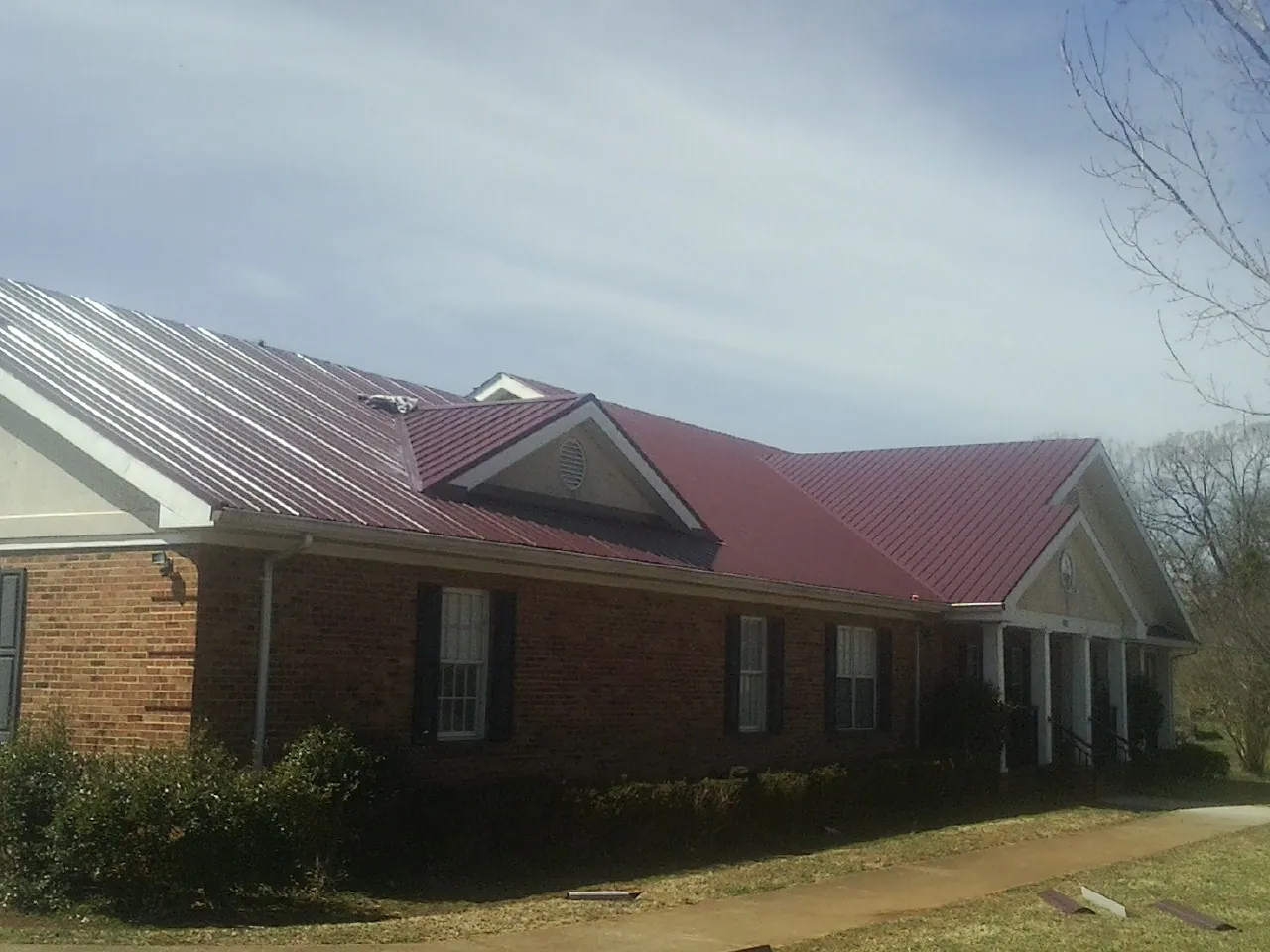 Red metal roof with gabled entries on a long brick building, from a Hail Damage Roof Repair job in Senecaville