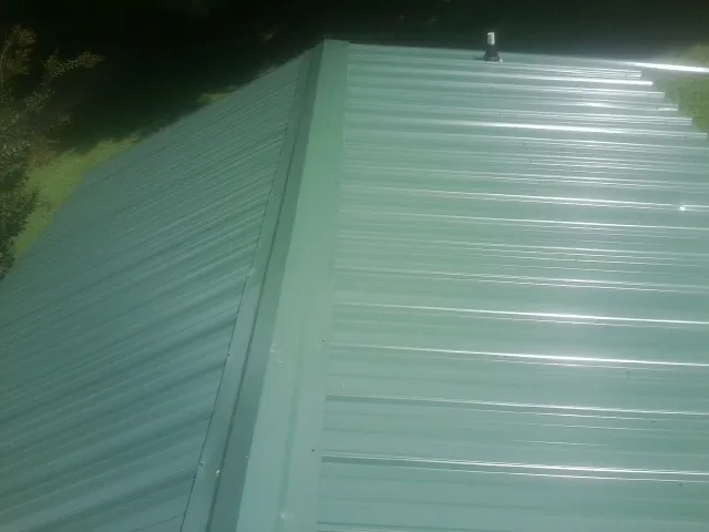 New green metal panels meeting at the ridge of a roof — Flat Roof Repair work by our crew in Senecaville