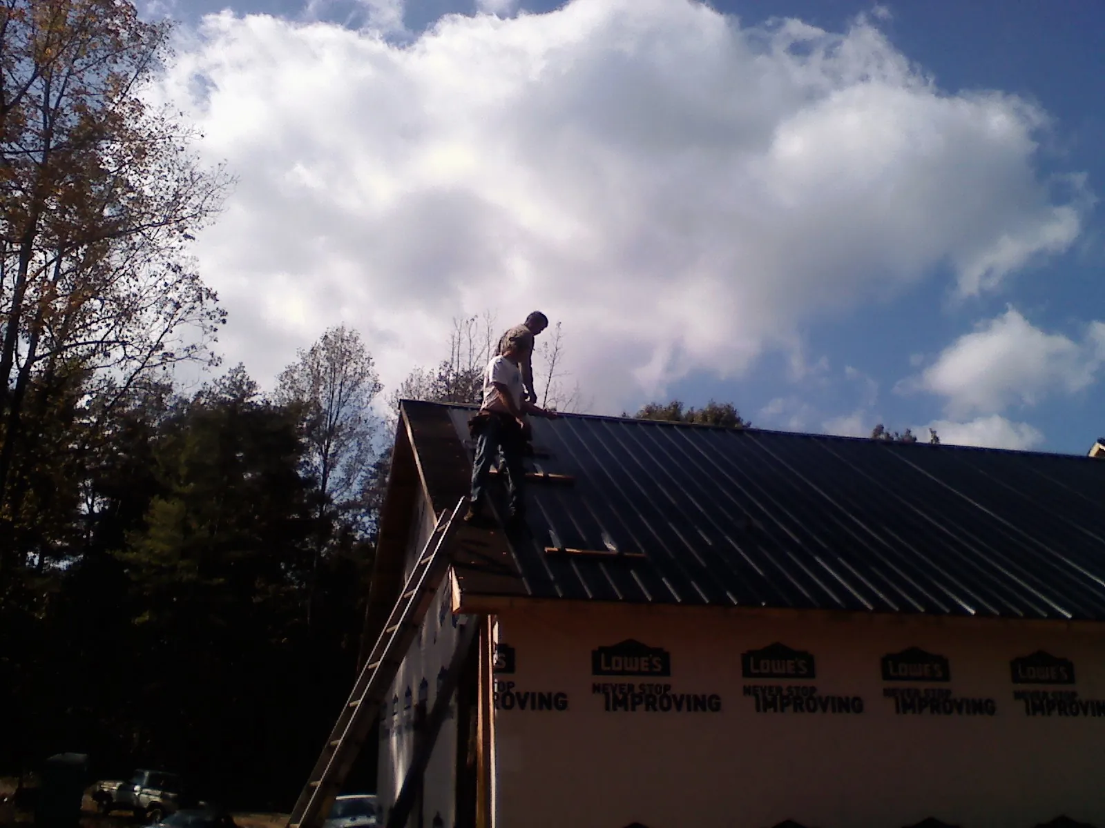 Roofer fastening dark metal panels high against a cloudy sky, from a Roof Inspection job in Senecaville