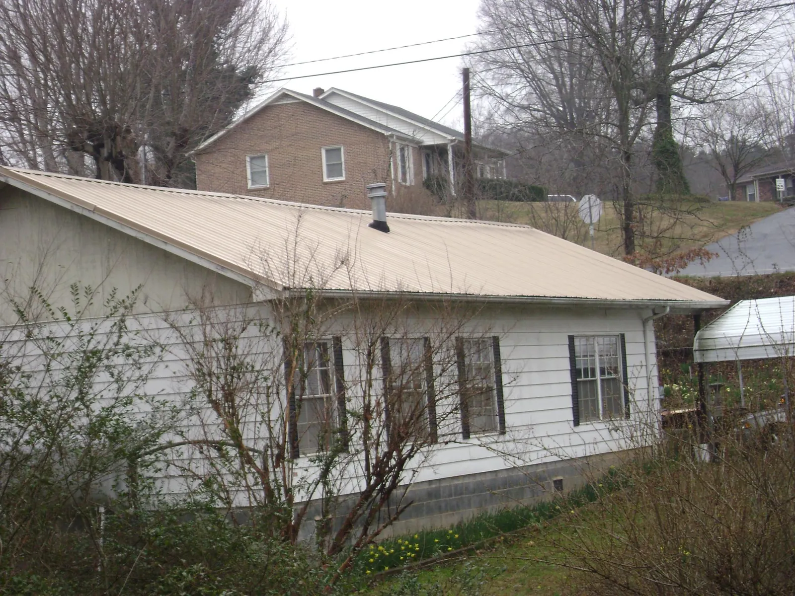 Tan metal roof on a white sided house set into a hillside — Commercial Roofing by Roofing Brothers in Senecaville